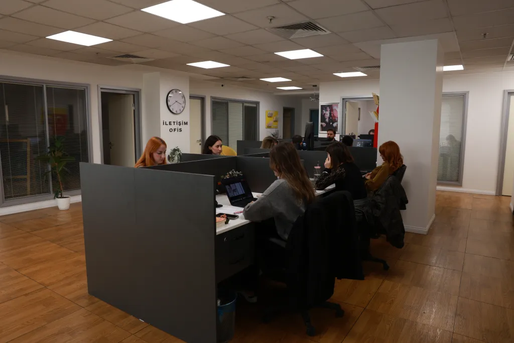 İletişim Media ofisi: ekip masa başında çalışıyor, duvarda İLETİŞİM OFİS yazısı